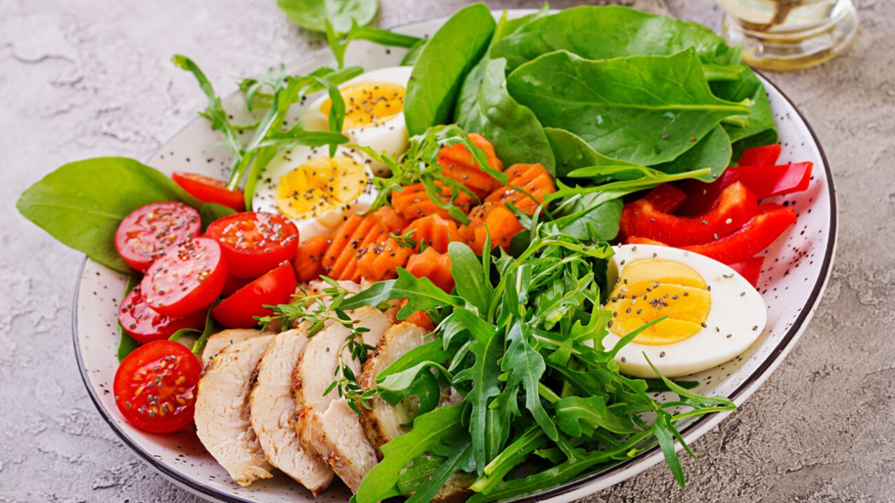 Plate with a keto diet food. Cherry tomatoes, chicken breast, eggs, carrot, salad with arugula  and spinach. Keto lunch