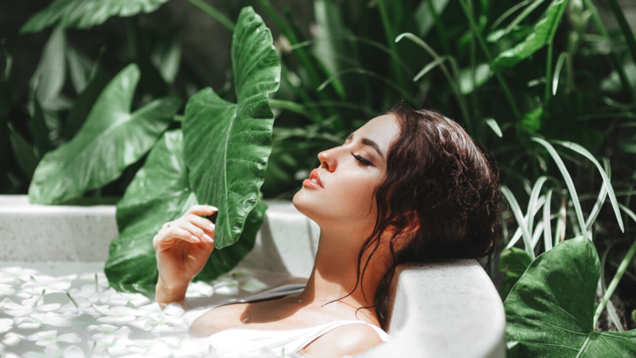Woman relaxing in round outdoor bath with tropical flowers, organic skin care, luxury spa hotel, lifestyle photo
