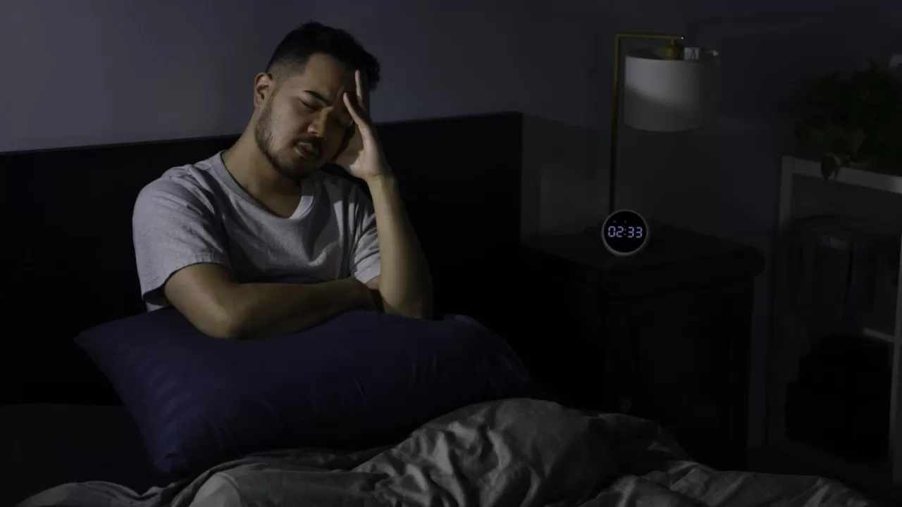 Depressed young Asian man sitting in bed cannot sleep from insomnia