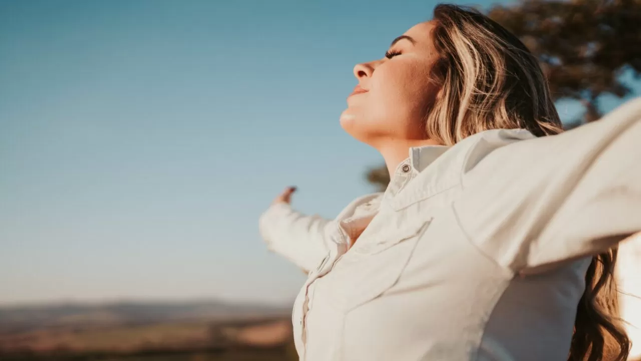 Latin woman at sunset breathing fresh air raising arms.